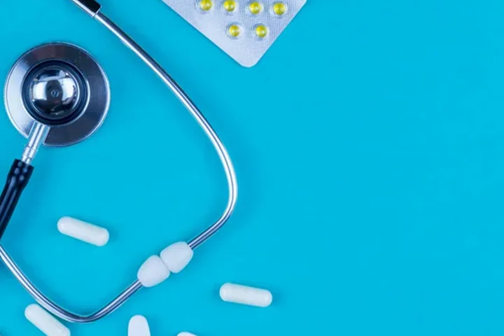 stethoscope with loose white pills at the bottom and pill package at the top