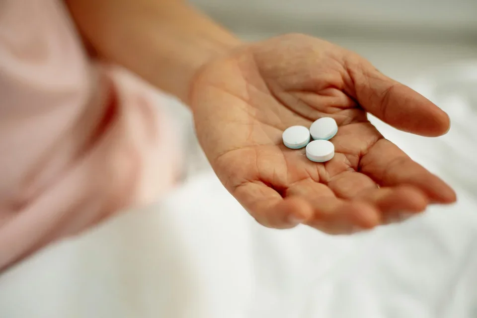 Hand with three white pill of person with a pink shirt in the background